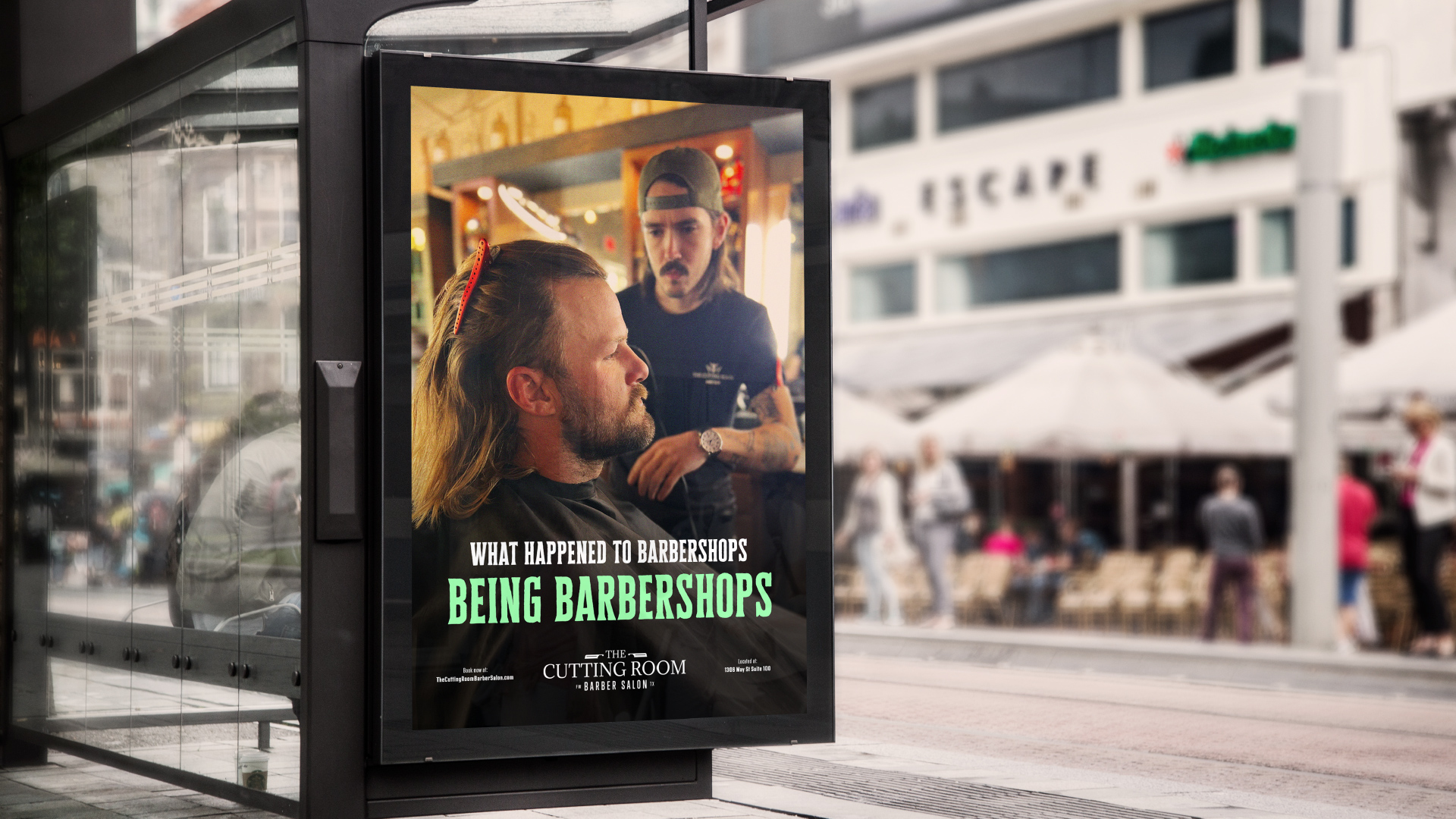 An ad shows a stylist giving someone a haircut with the text, “What happened to barbershops being barbershops.” The ad is featured at a bus stop along a busy street.