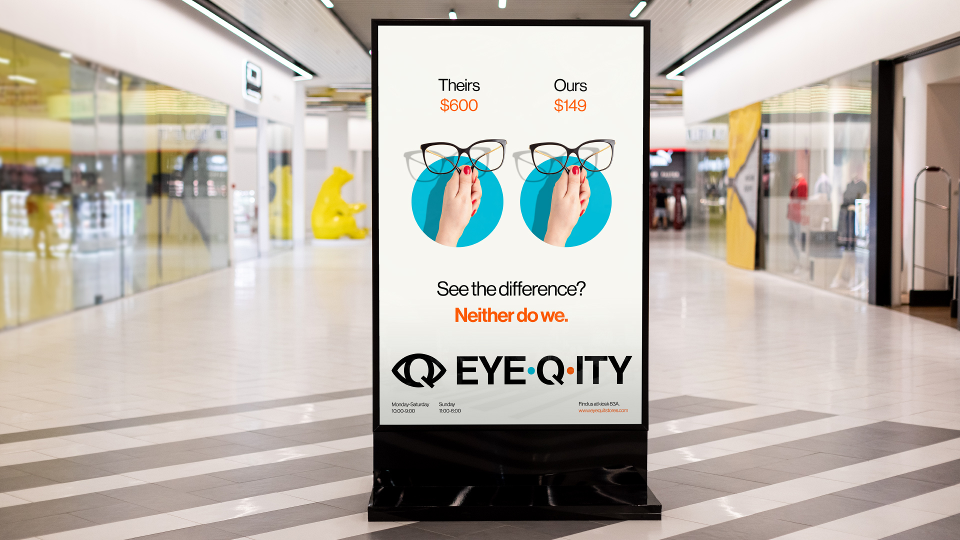 An ad on mall signage sits in between rows of stores. The ad shows hands holding up the same pair of glasses. The one on the left has a $600 price tag. The one on the right has a $149 price tag. The text below says, “See the difference? Neither do we.” The logo is below it.