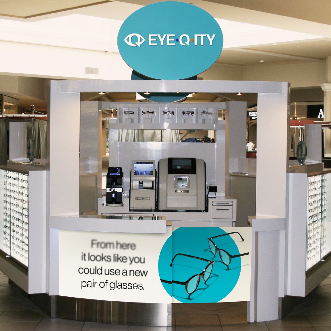 An EYEQ.ITY kiosk features the new logo. The text below the front counter says, “From here it looks like you could use a new pair of glasses.” The text goes from fuzzy to crisp. Two pairs of glasses are next to it.
