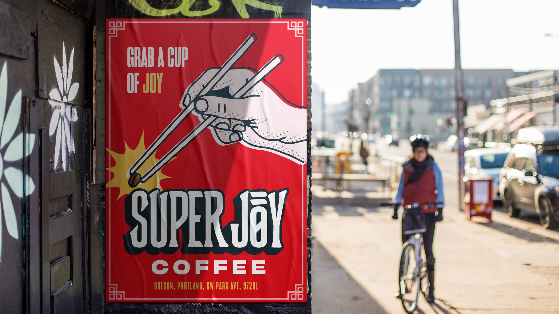 In the foreground, there’s a Super Joy Coffee poster. It’s got a similar design to the bag of coffee with a hand, chopsticks, and coffee bean. In the background is a bicyclist riding down a city street.